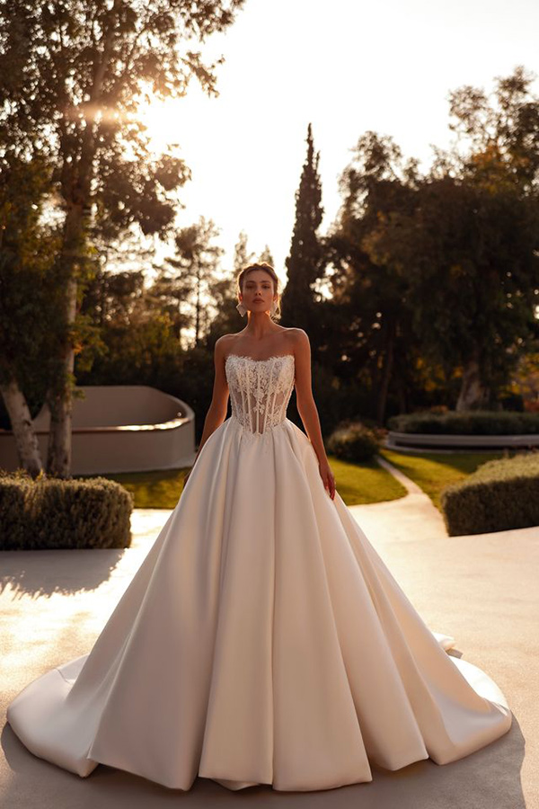Eine Frau im eleganten Brautkleid mit Spitzenoberteil steht entspannt im Garten