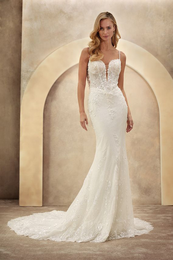 Eine blonde Frau mit sanftem Lächeln trägt ein elegantes helles Spitzenbrautkleid