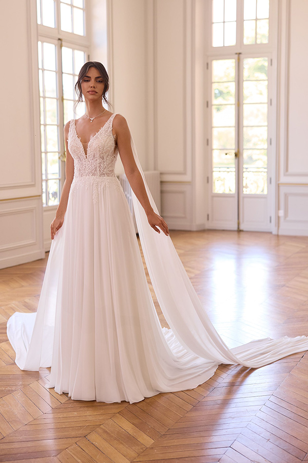 Eine junge Frau mit ernstem Blick trägt ein elegantes weißes Brautkleid mit Schleppe