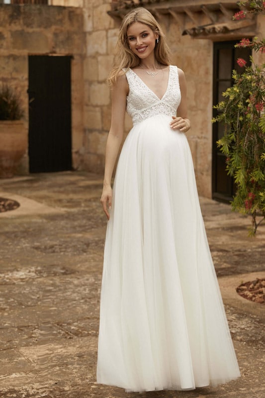 Eine lächelnde schwangere Frau in einem eleganten weißen Kleid mit Spitzendetails