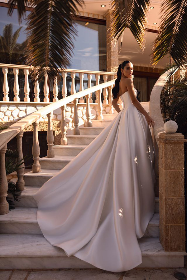 Eine elegante Frau mit ernstem Blick trägt ein weißes, wallendes Abendkleid auf Marmortreppe
