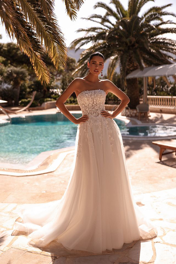 Eine Frau mit ernster Miene trägt ein weißes schulterfreies Brautkleid am Pool