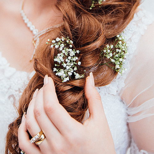 Eine Frau mit langen roten Haaren und Blumen im Zopf trägt ein weißes Kleid