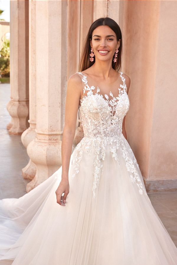 Junge Frau mit langem braunem Haar lächelt im cremefarbenen Spitzenkleid