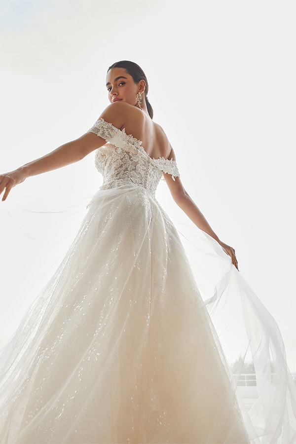 Eine junge Frau im weißen Spitzen-Brautkleid schaut mit ernstem Blick über die Schulter