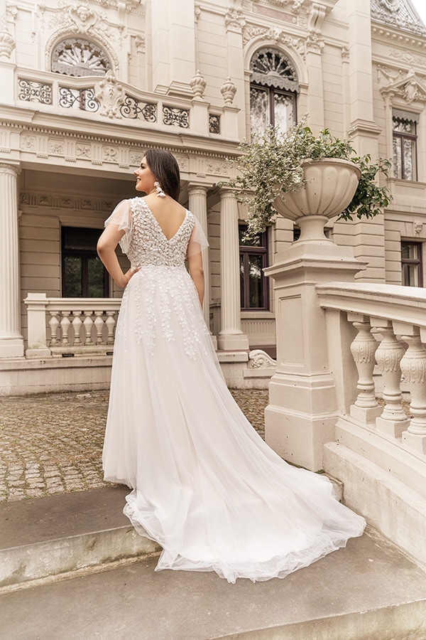 Eine Frau steht in einem weißen Brautkleid mit Spitze und blickt zur Seite