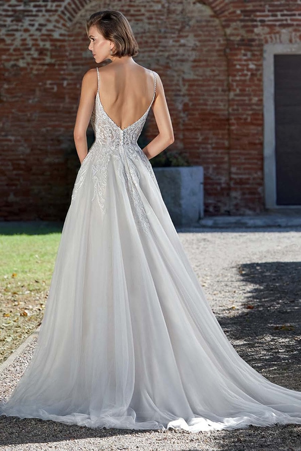 Eine Frau mit kurzem, braunem Haar trägt ein elegantes, weißes Brautkleid mit tiefem Rückenausschnitt