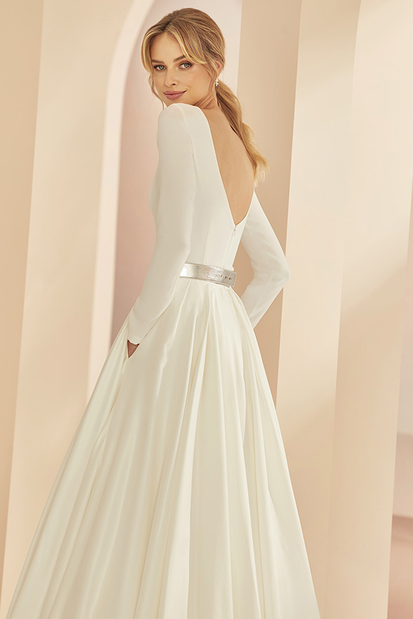 Junge Frau mit blonden Haaren lächelt dezent in elegantem cremefarbenem Kleid