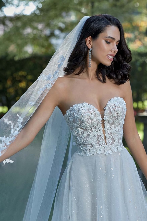 Junge Frau mit langem dunklem Haar lächelt im floralen Brautkleid mit Spitzendetails