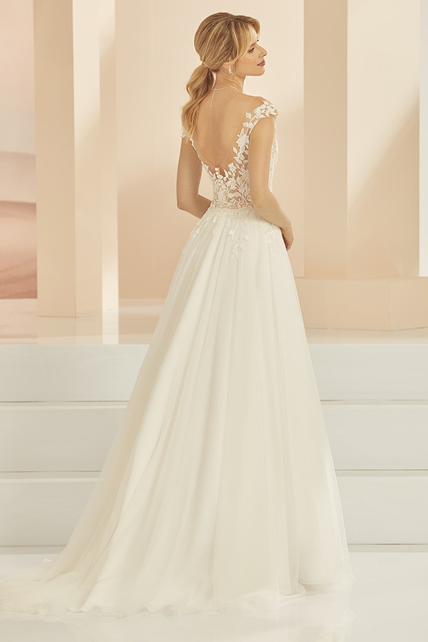 Eine Frau mit blondem Pferdeschwanz trägt ein cremefarbenes Brautkleid mit Spitze