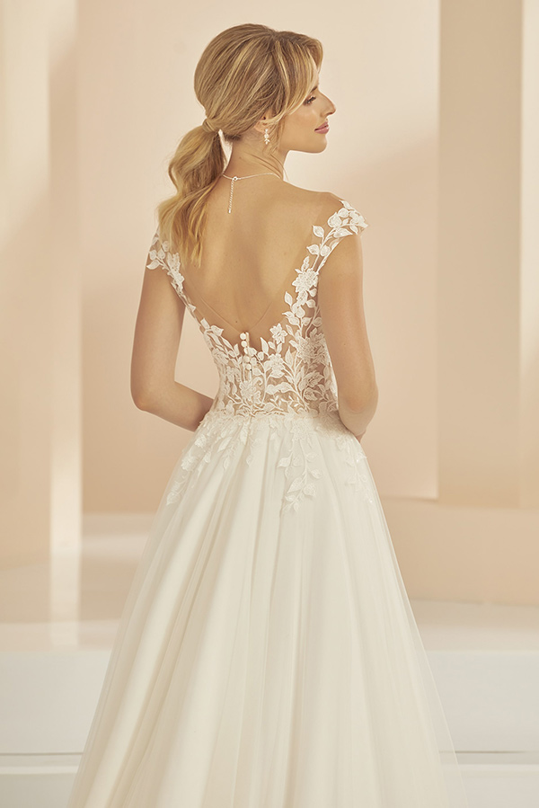 Junge Frau mit blondem Pferdeschwanz trägt weißes Spitzenkleid mit tiefem Rückenausschnitt