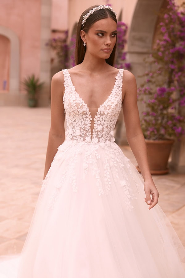 Junge Frau mit seriösem Blick trägt ein weißes Brautkleid mit floraler Spitze