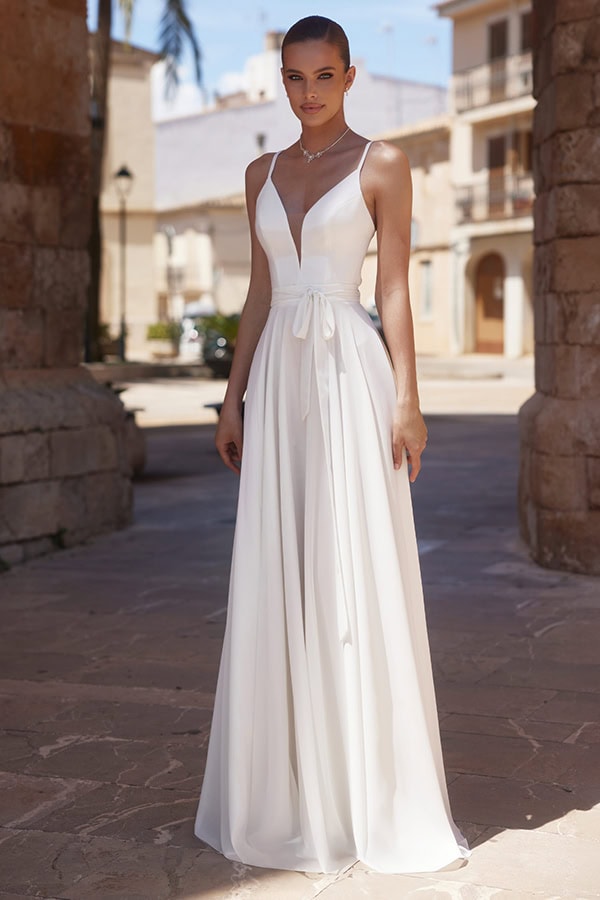 Eine junge Frau mit ernstem Blick trägt ein elegantes weißes Kleid mit Schleife