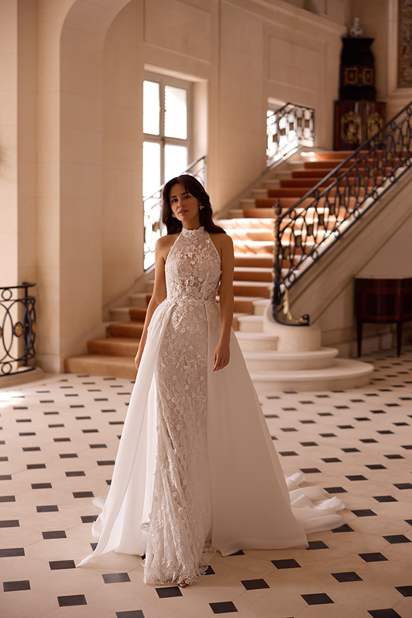 Frau im eleganten cremefarbenen Brautkleid steht gelassen vor prachtvoller Treppe
