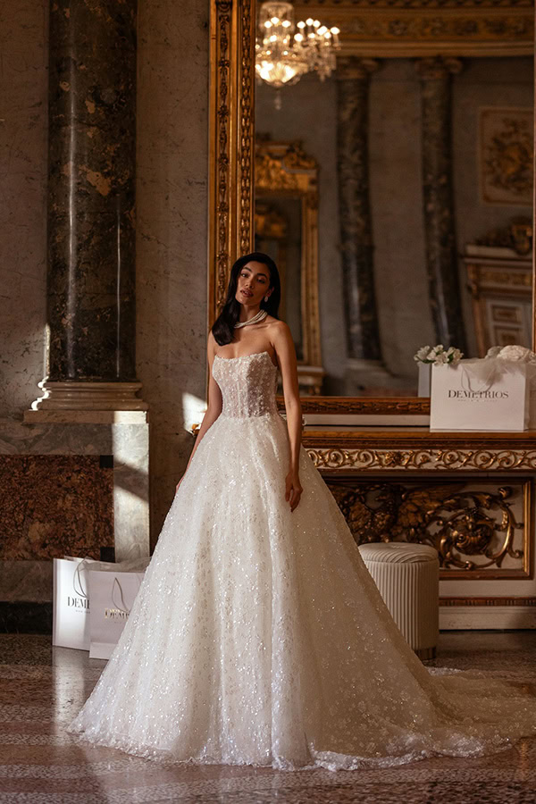 Eine elegante Frau mit langem dunklem Haar steht ernst in prachtvollem weißen Brautkleid