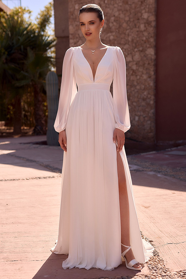 Junge Frau mit elegantem weißen Kleid lächelt leicht im Sonnenschein mit Beinschlitz