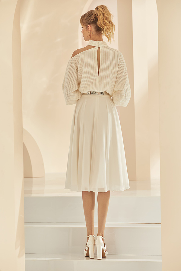 Eine blonde Frau im eleganten cremefarbenen Kleid steht aufrecht mit lockerem Haar