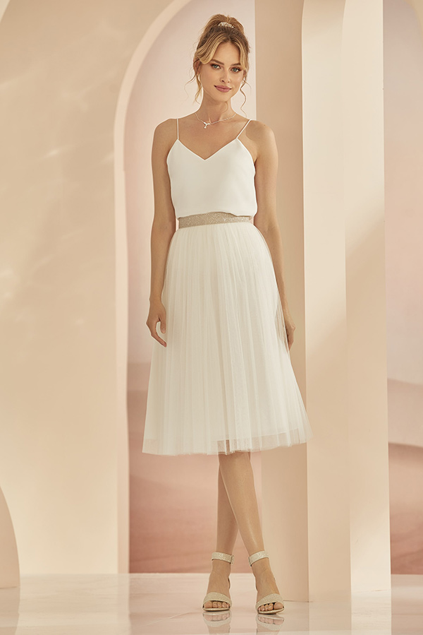 Eine junge Frau mit freundlichem Blick trägt ein weißes Kleid und Sandaletten