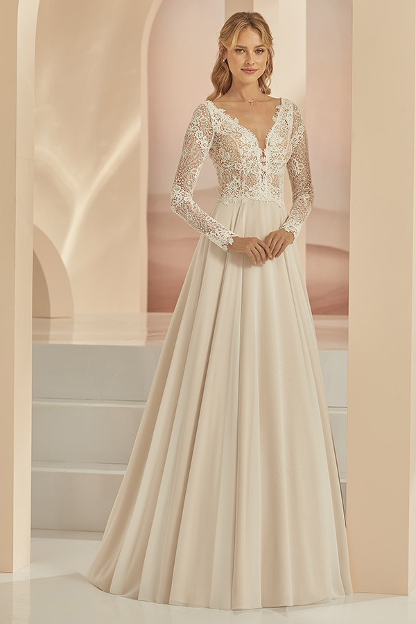 Eine blonde Frau mit sanftem Lächeln trägt ein elegantes cremefarbenes Brautkleid