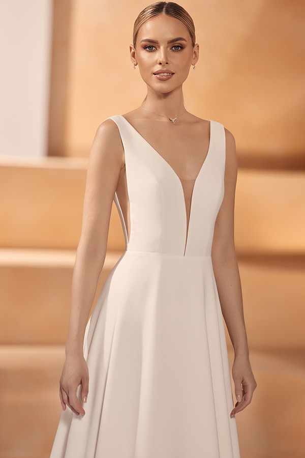 Eine junge Frau mit elegantem weißem Kleid und dezenter Kette lächelt freundlich