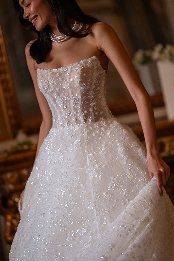 Eine lächelnde Frau im schimmernden weißen Kleid mit Perlenkette und Blumenmuster