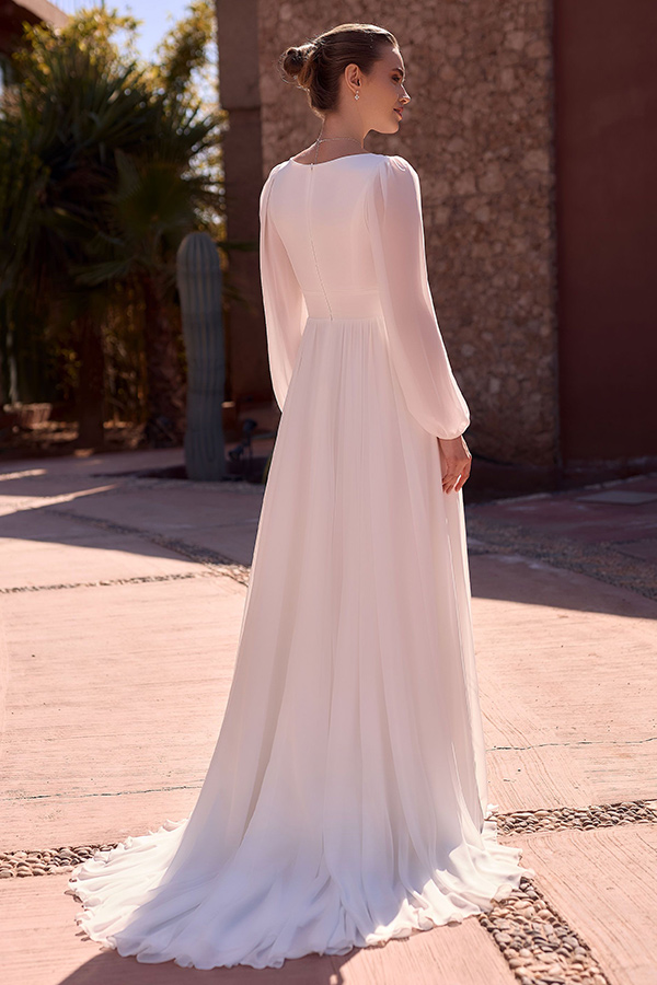 Eine Frau mit elegantem Dutt trägt ein langes weißes Kleid und schaut entspannt zurück