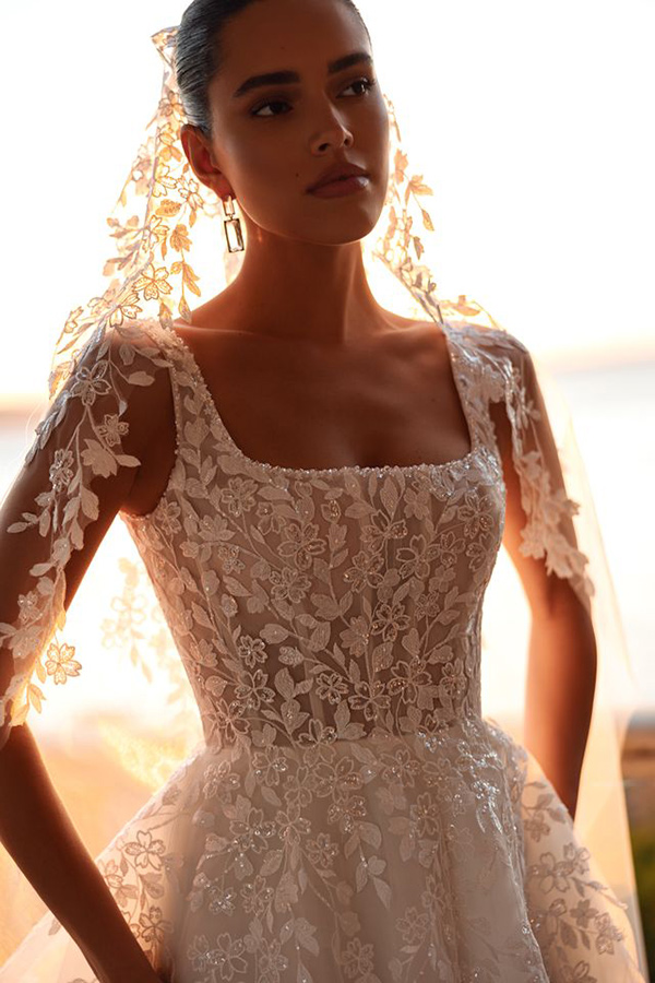 Junge Frau mit ernstem Blick trägt cremefarbenes Brautkleid aus Spitze mit Blumenmuster