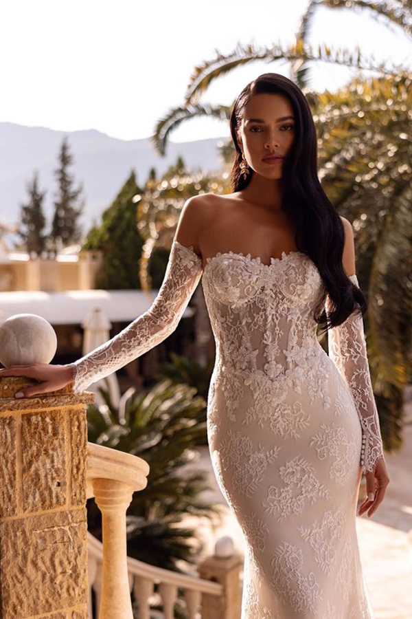 Eine junge Frau mit langen dunklen Haaren steht ernst in einem weißen Spitzenkleid