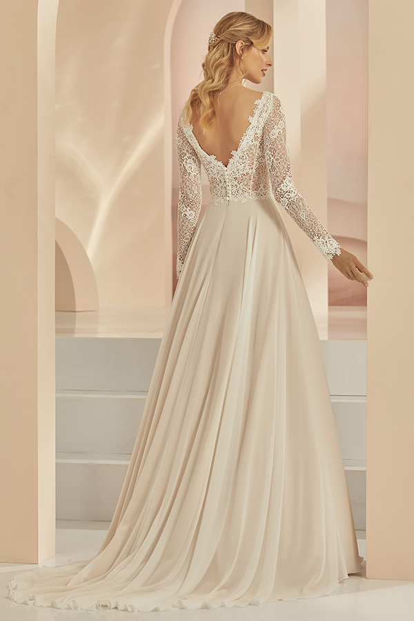 Eine blonde Frau in cremefarbenem Brautkleid mit Spitze steht elegant auf weißen Stufen