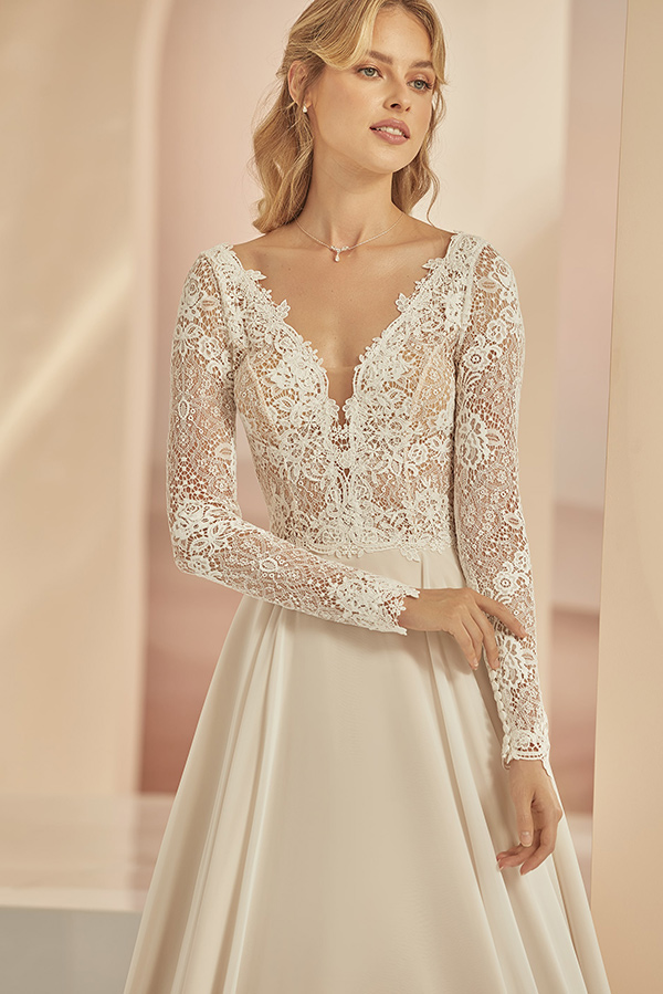 Junge Frau mit blondem Haar lächelt leicht und trägt elegantes Brautkleid in Creme