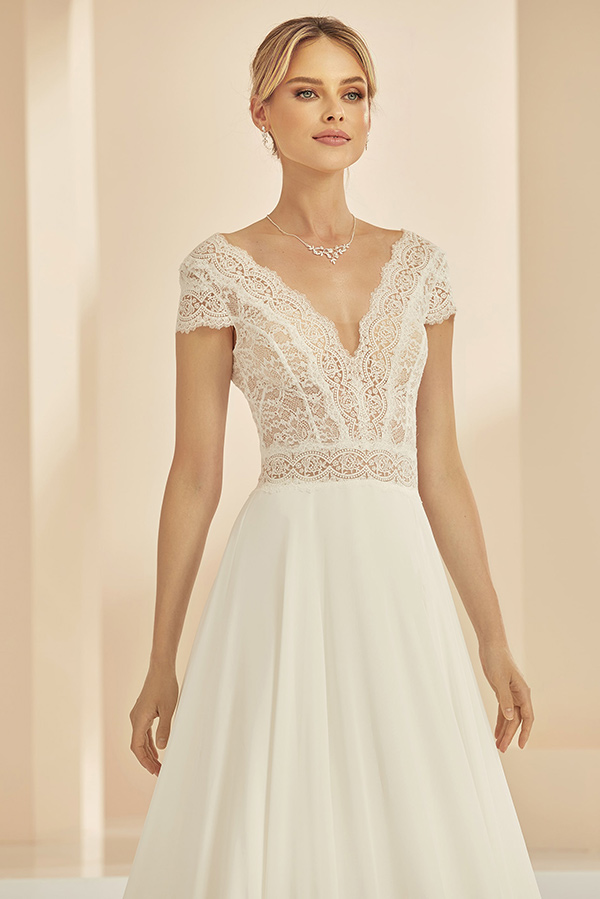 Eine blonde Frau lächelt sanft in einem eleganten cremefarbenen Spitzenkleid