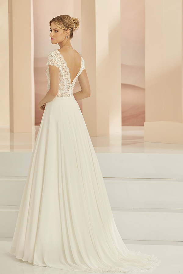 Eine blonde Frau in einem eleganten weißen Brautkleid mit Spitzenrücken steht ruhig