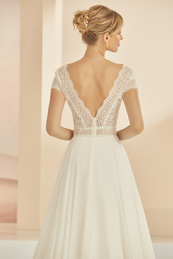 Eine blonde Frau im Spitzenbrautkleid steht mit eleganter Hochsteckfrisur