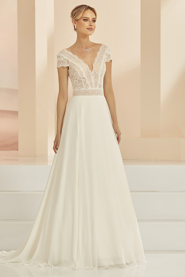 Eine junge Frau mit elegantem Lächeln trägt ein cremeweißes Brautkleid mit Spitzenoberteil