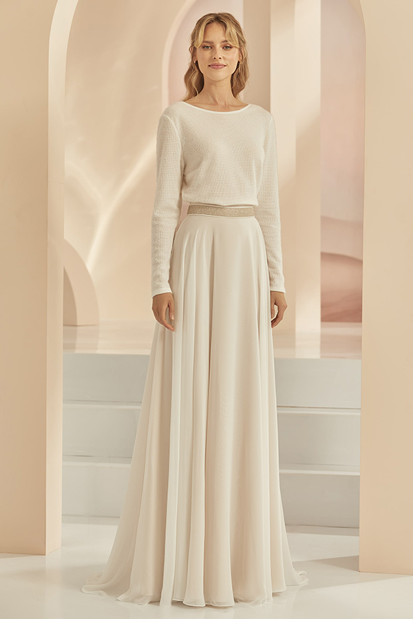 Blonde Frau mit sanftem Lächeln trägt ein cremefarbenes langes Kleid in elegantem Raum