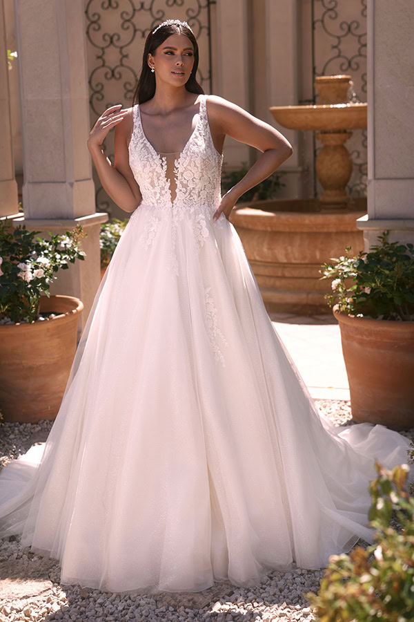 Eine Frau mit langem dunklem Haar trägt ein weißes Brautkleid mit Spitzendetails und Blickfang-Ausschnitt