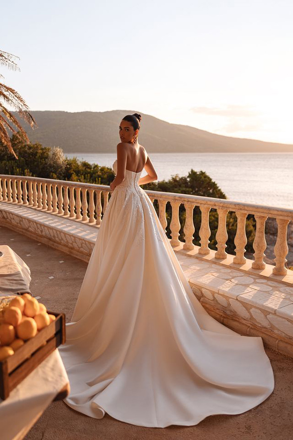 Eine elegante Frau im weissen Brautkleid blickt ernst über das Meer bei Sonnenuntergang