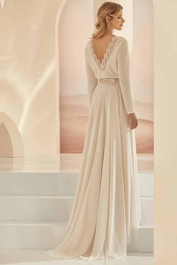 Eine blonde Frau in einem cremefarbenen Spitzenkleid steht verträumt auf weißen Stufen