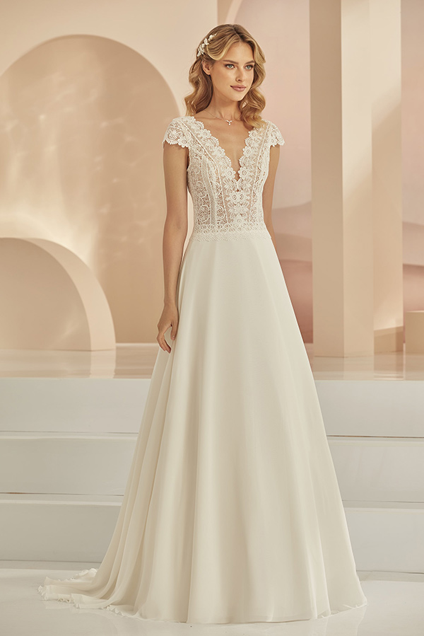 Junge Frau mit blondem Haar in einem weißen Brautkleid mit Spitzenoberteil und sanftem Lächeln