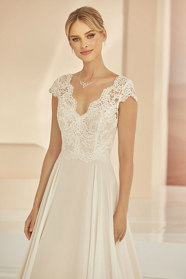 Junge Frau mit sanftem Lächeln in cremefarbenem Spitzenkleid und dezenter Kette