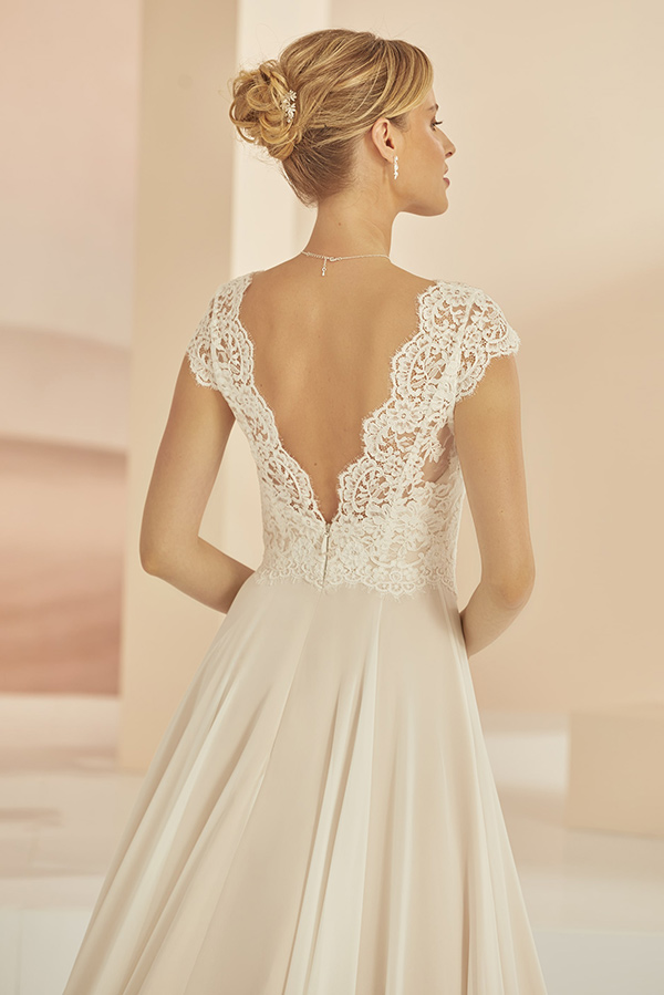 Blonde Frau im eleganten cremefarbenen Brautkleid mit Spitzenrücken und Hochsteckfrisur