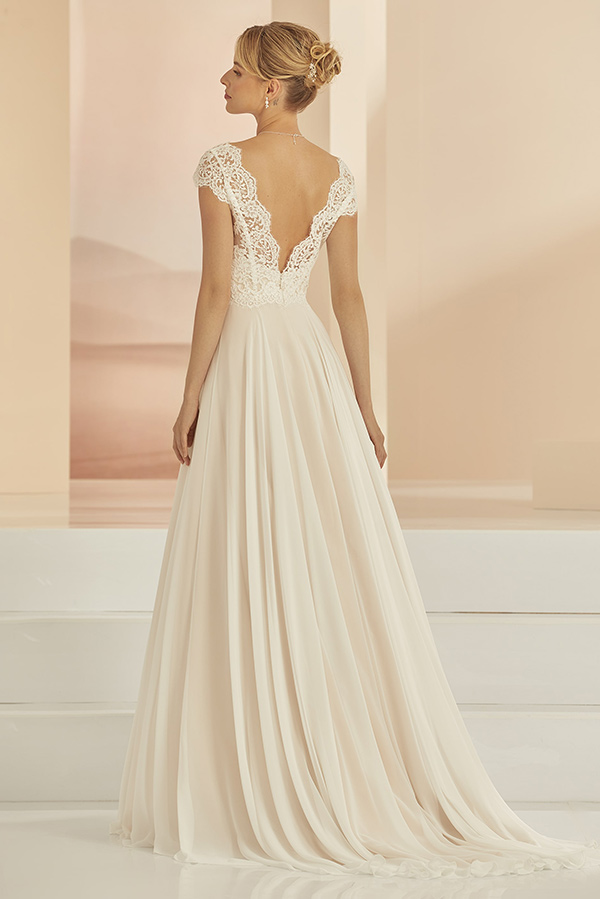 Eine blonde Frau in cremefarbenem Spitzenkleid blickt elegant nach links