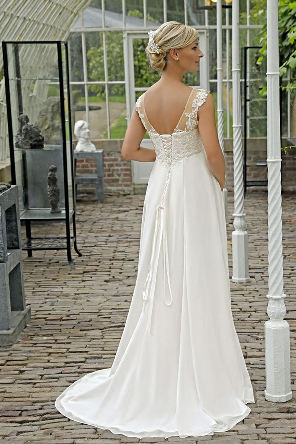 Blonde Frau im eleganten weißen Hochzeitskleid steht lächelnd im Gewächshaus