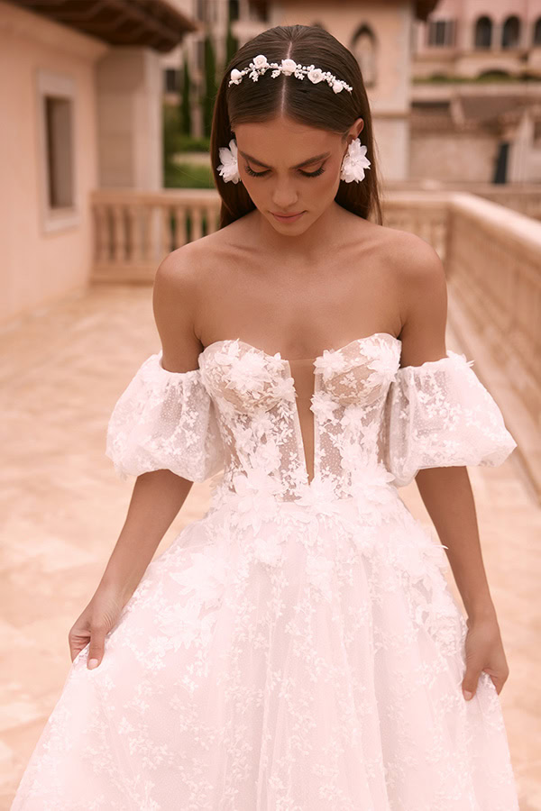 Eine junge Frau mit ernstem Blick trägt ein elegantes weißes Spitzenkleid mit Puffärmeln