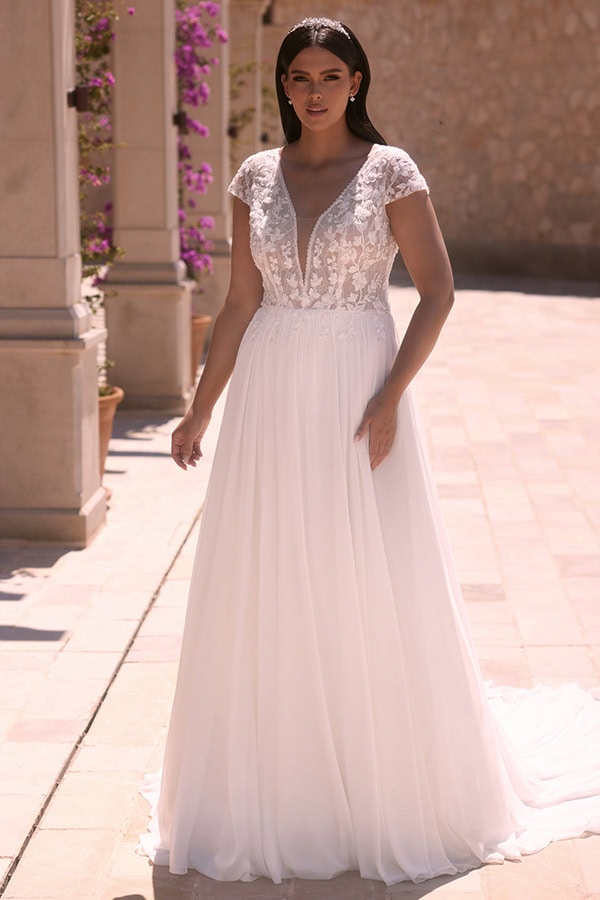 Eine braunhaarige Frau mit neutralem Ausdruck trägt ein weißes elegantes Brautkleid