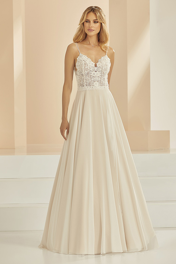 Eine blonde Frau mit sanftem Lächeln trägt ein elegantes cremefarbenes Spitzenkleid