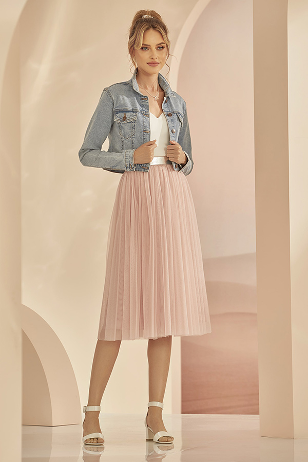 Junge Frau mit sanftem Lächeln trägt eine blaue Jeansjacke und einen rosa Faltenrock