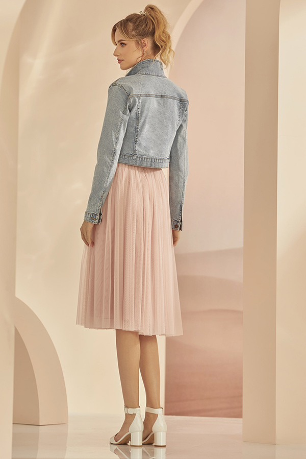 Junge Frau lächelt leicht und trägt eine Jeansjacke mit rosafarbenem Chiffonrock