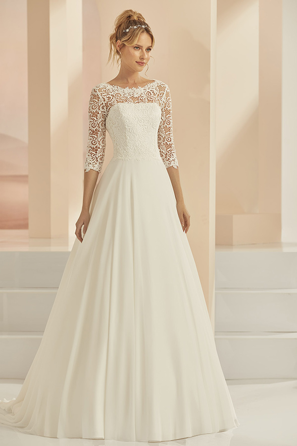 Eine lächelnde Frau trägt ein elegantes weißes Brautkleid mit Spitzenärmeln