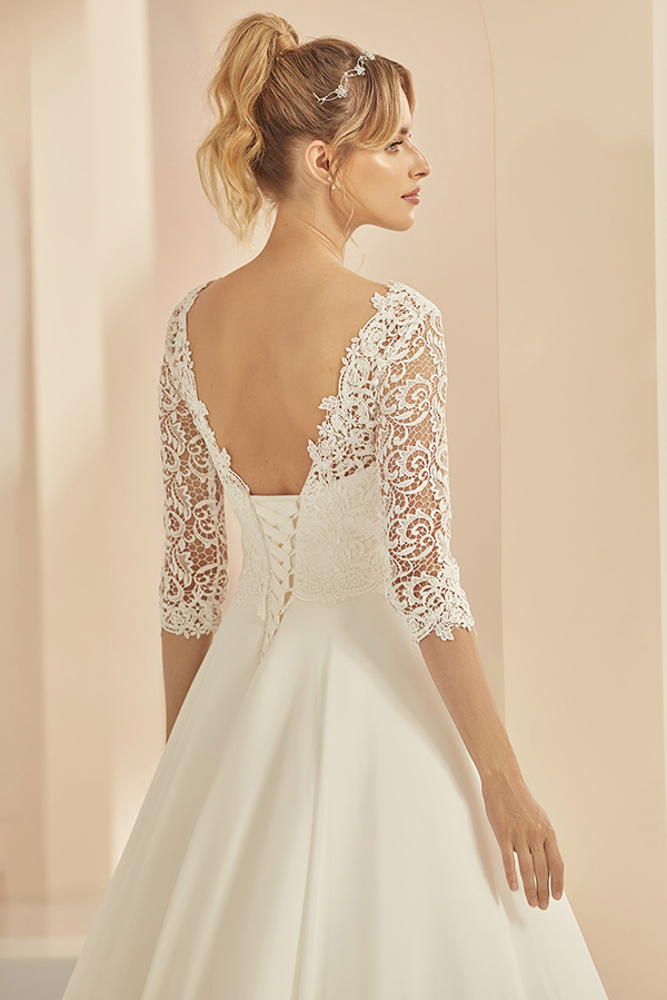 Junge Frau mit elegantem Dutt trägt ein weißes Brautkleid mit Spitzenärmeln und offenem Rücken